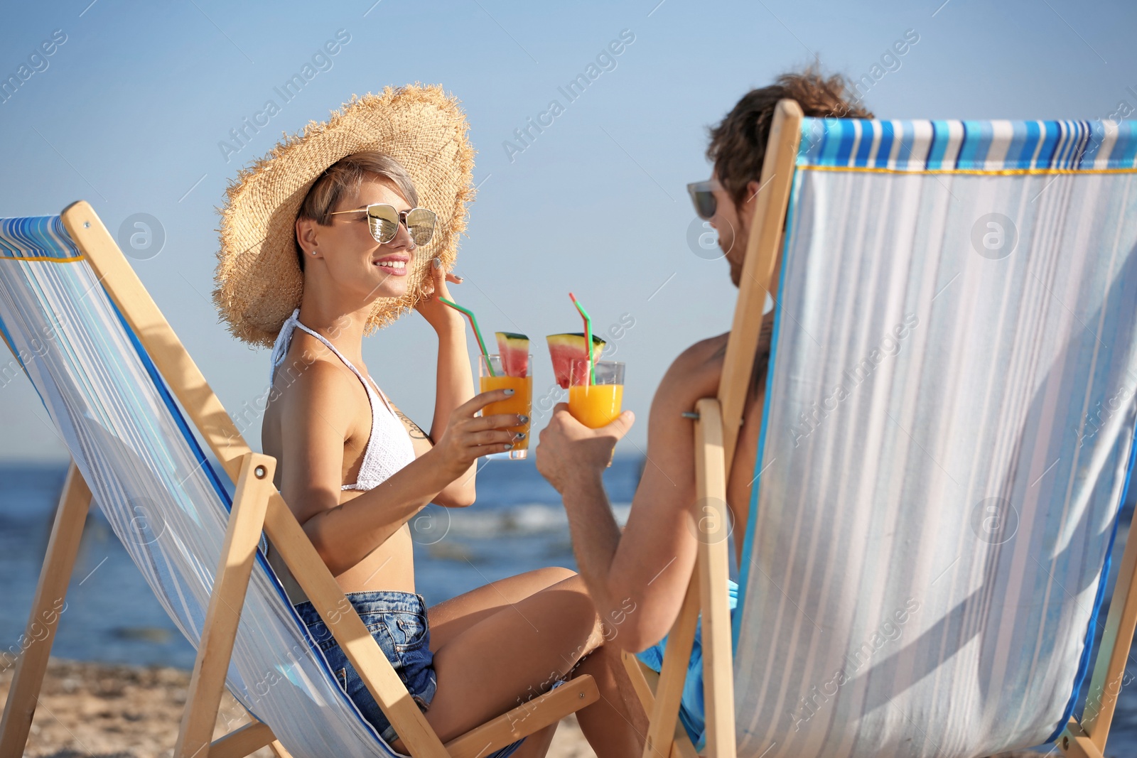 Photo of Young couple with cocktails in beach chairs at seacoast