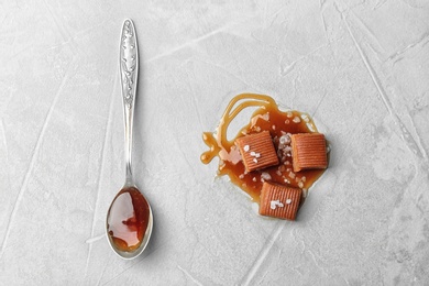 Photo of Spoon and candies with salted caramel sauce on light background, top view