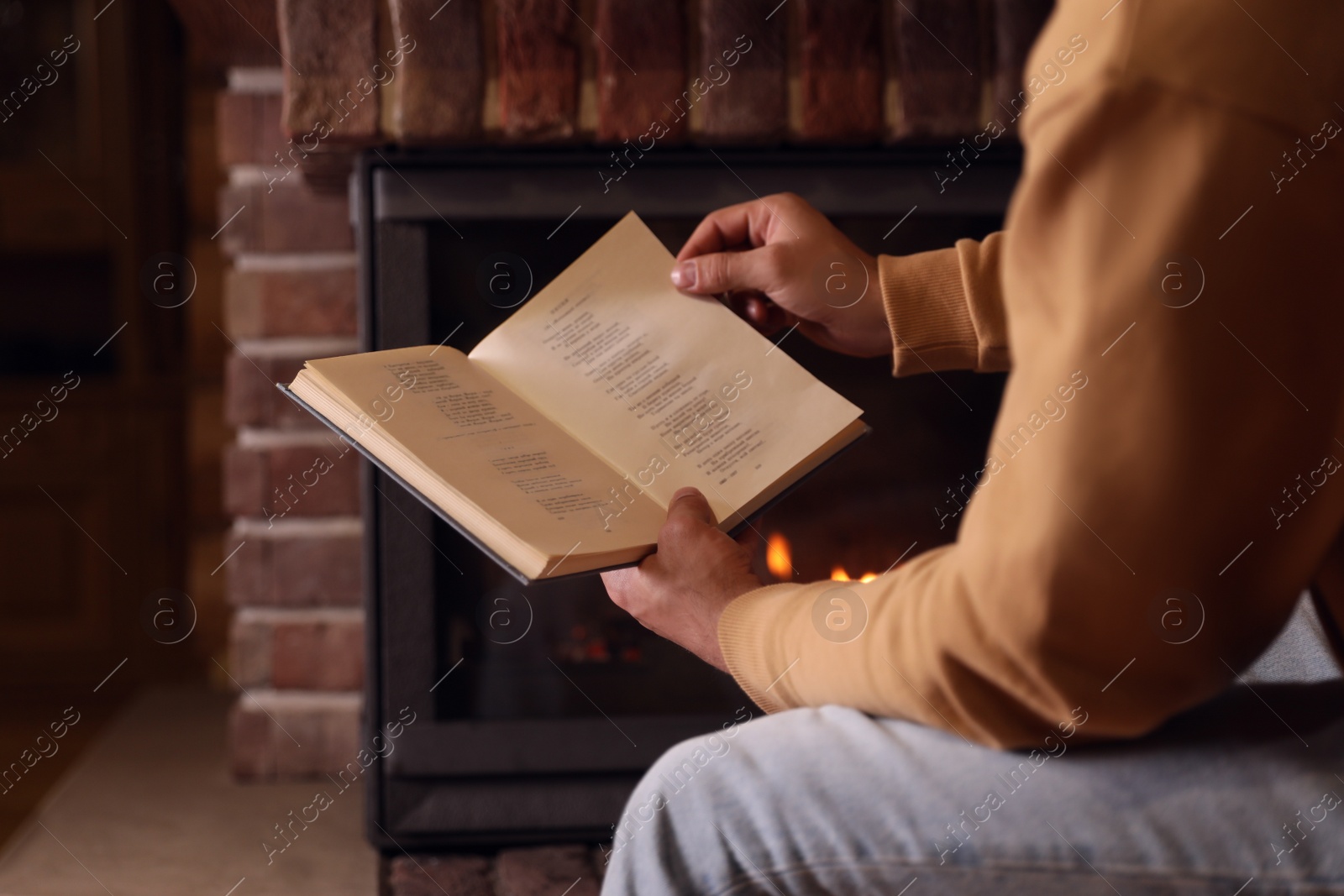 Photo of Man reading book near fireplace at home, closeup