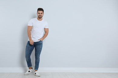 Photo of Young man in stylish jeans near light wall. Space for text