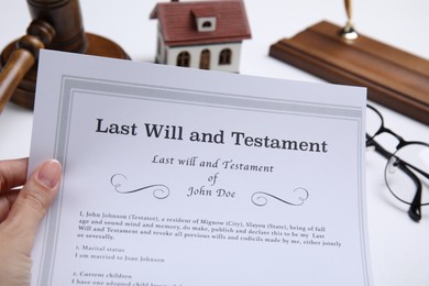 Photo of Woman holding last will and testament at white table, closeup