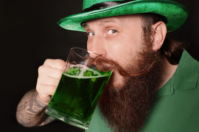 Photo of Bearded man drinking green beer on black background. St. Patrick's Day celebration