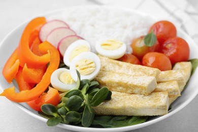 Delicious poke bowl with basil, vegetables, eggs and tofu on light grey table, closeup