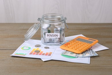 Photo of Glass jar with word Pension, coins, dollar banknotes and calculator on wooden table