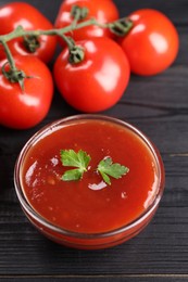 Photo of Delicious ketchup in bowl and tomatoes on black wooden table, closeup. Tomato sauce