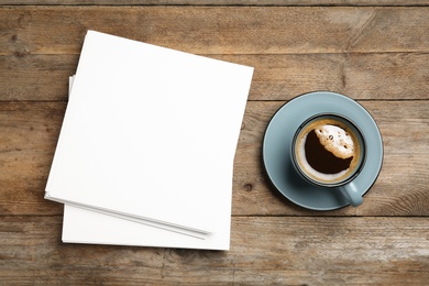 Blank paper sheets for brochure and cup of coffee on wooden background, flat lay. Mock up