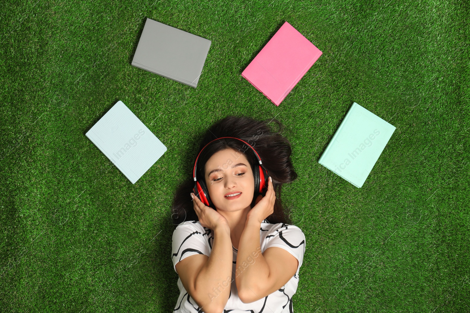 Photo of Young woman listening to audiobook while lying on grass, flat lay