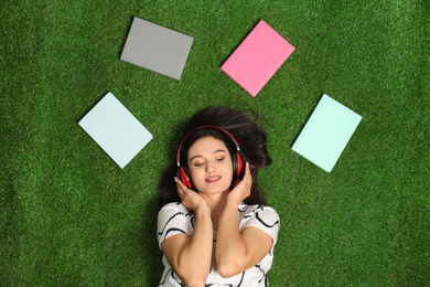 Photo of Young woman listening to audiobook while lying on grass, flat lay