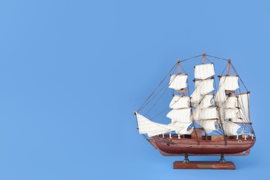 Photo of Miniature model of old ship with white sails on blue background, space for text