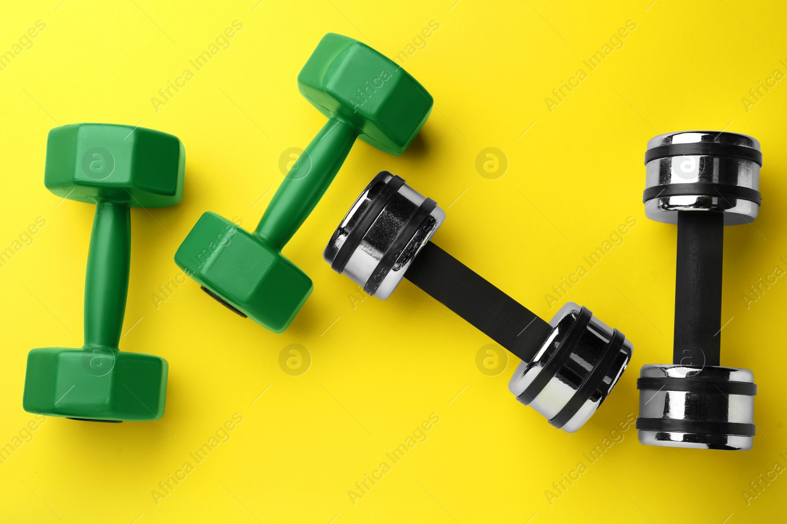 Photo of Many different stylish dumbbells on yellow background, flat lay