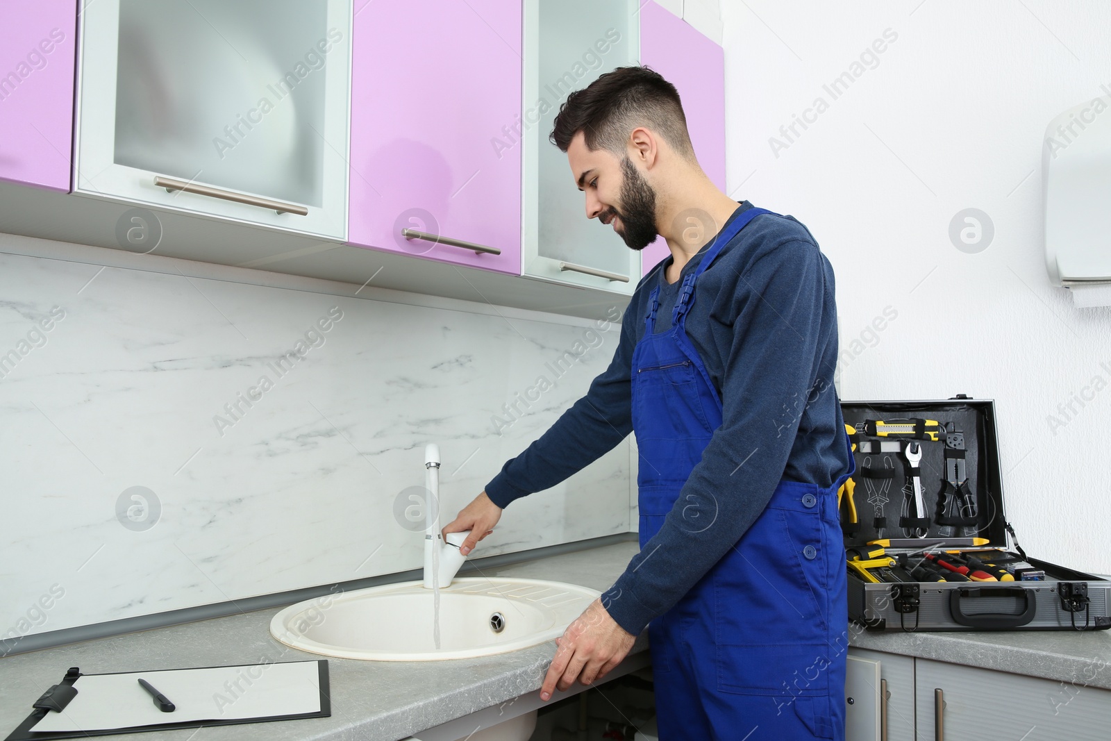 Photo of Male plumber in uniform checking faucet in kitchen. Repair service