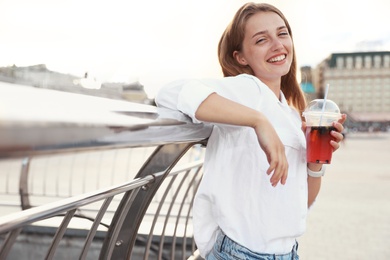 Photo of Young woman with refreshing drink on city street. Space for text