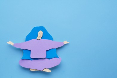 Photo of Woman paper figure on light blue background, top view. Space for text