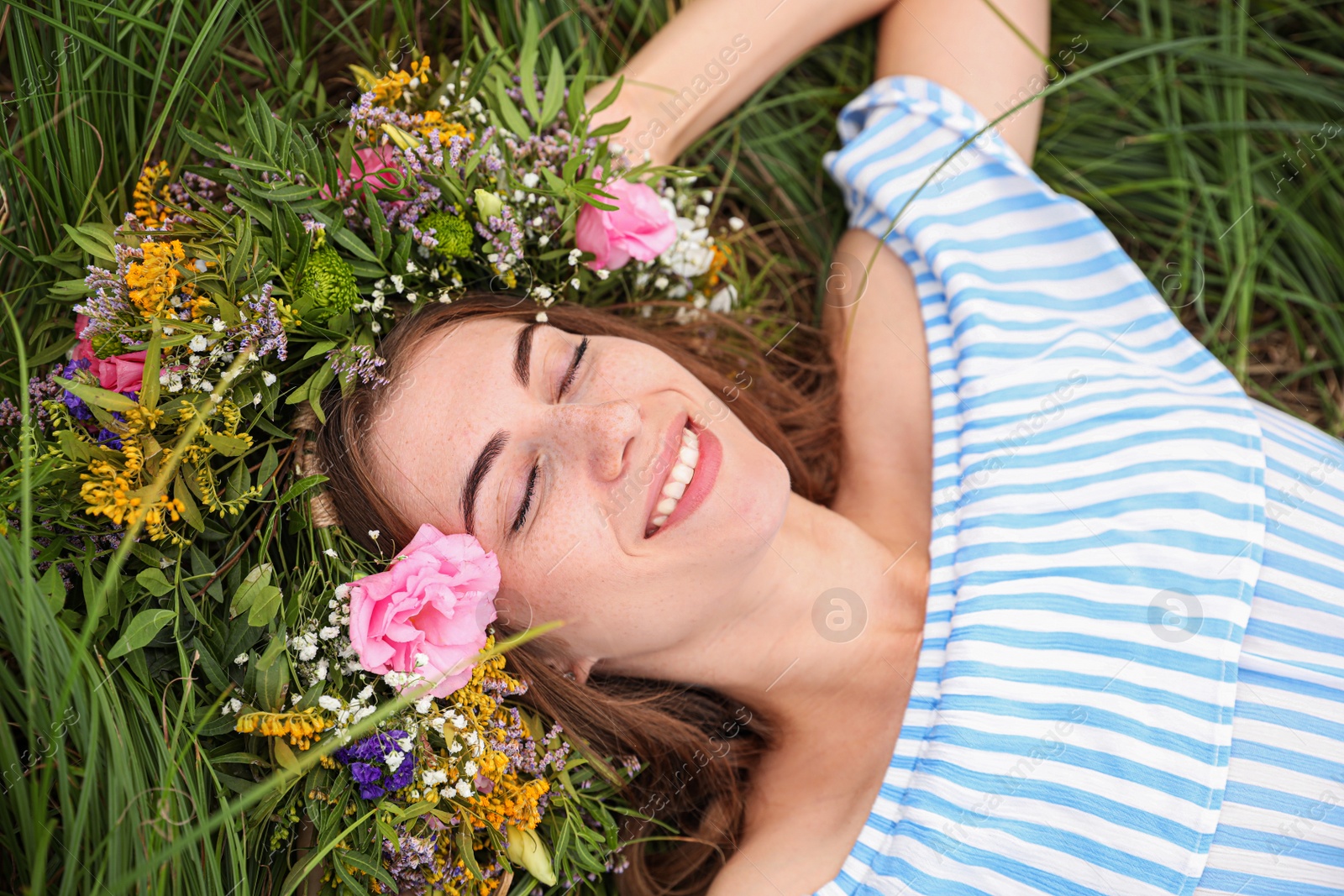 Photo of Young woman wearing wreath made of beautiful flowers on green grass