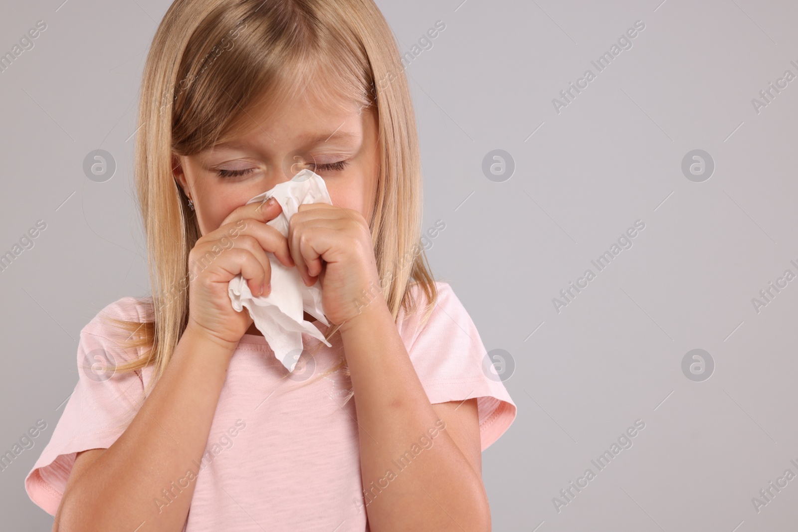 Photo of Suffering from allergy. Little girl with tissue sneezing on light gray background, space for text