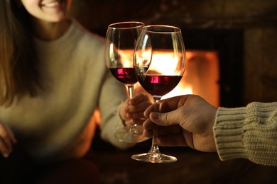 Couple clinking glasses of wine near fireplace at home, closeup