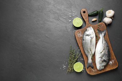 Flat lay composition with raw dorada fish on black table, space for text