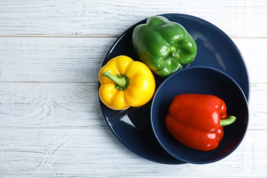 Photo of Dishware with ripe paprika peppers on white wooden background, top view