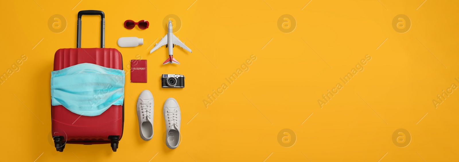 Image of COVID-19 pandemic, travel during coronavirus outbreak. Suitcase with protective mask and accessories on yellow background, flat lay 