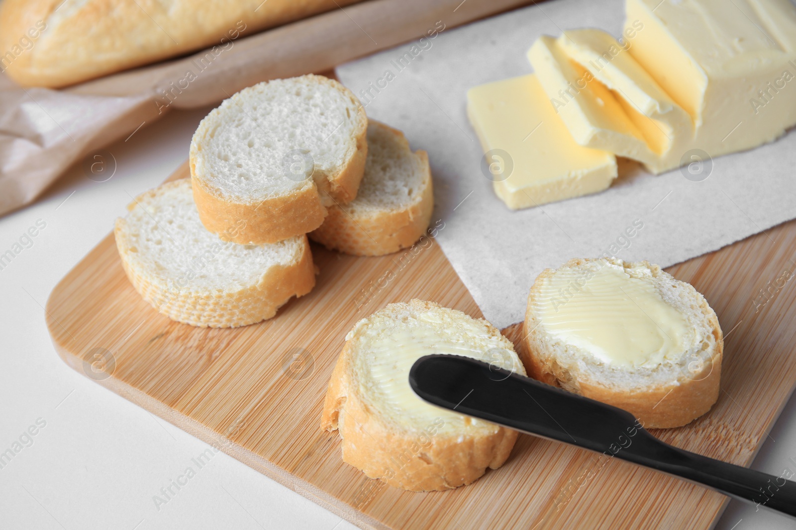 Photo of Tasty cut baguette with fresh butter on white table, closeup