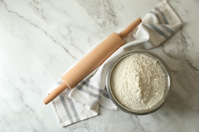 Photo of Flour in bowl, rolling pin and napkin on white marble table, top view. Space for text