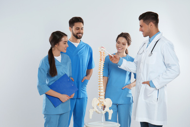 Photo of Professional orthopedist with human spine model teaching medical students against light background