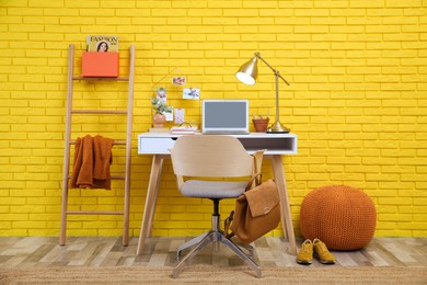 Stylish home office interior with comfortable workplace near yellow brick wall