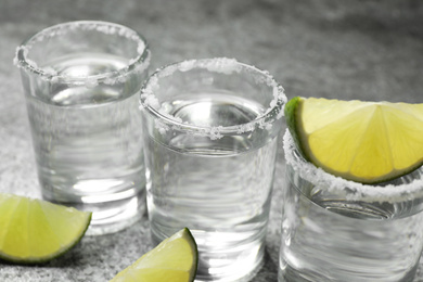 Photo of Mexican Tequila shots with salt and lime slices on grey table, closeup
