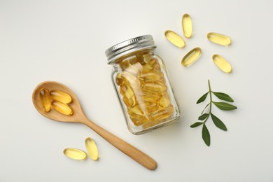 Bottle, vitamin capsules, spoon and leaves on white background, flat lay