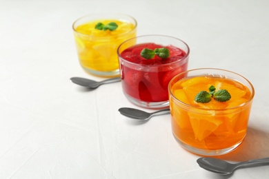 Glass bowls of natural jelly desserts on light table, space for text