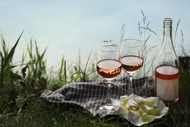 Photo of Delicious rose wine, cheese and grapes on picnic blanket near lake, space for text