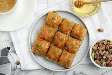 Photo of Delicious sweet baklava with pistachios, honey and aromatic coffee on white marble table, flat lay