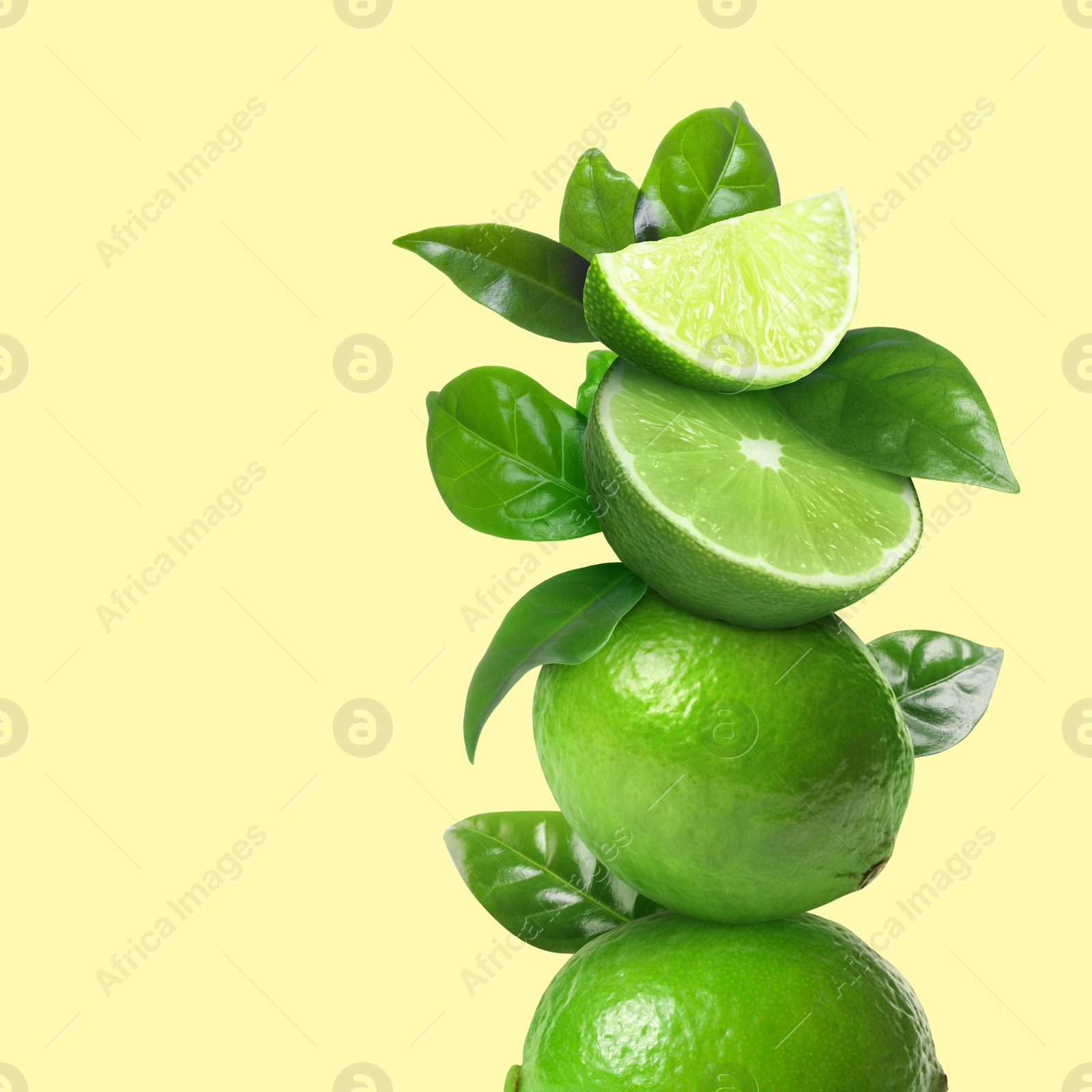 Image of Stacked cut and whole limes with green leaves on pale light yellow background, space for text