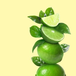 Image of Stacked cut and whole limes with green leaves on pale light yellow background, space for text