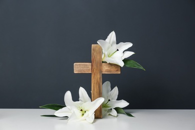 Photo of Composition with wooden cross and blossom lilies on table against color background