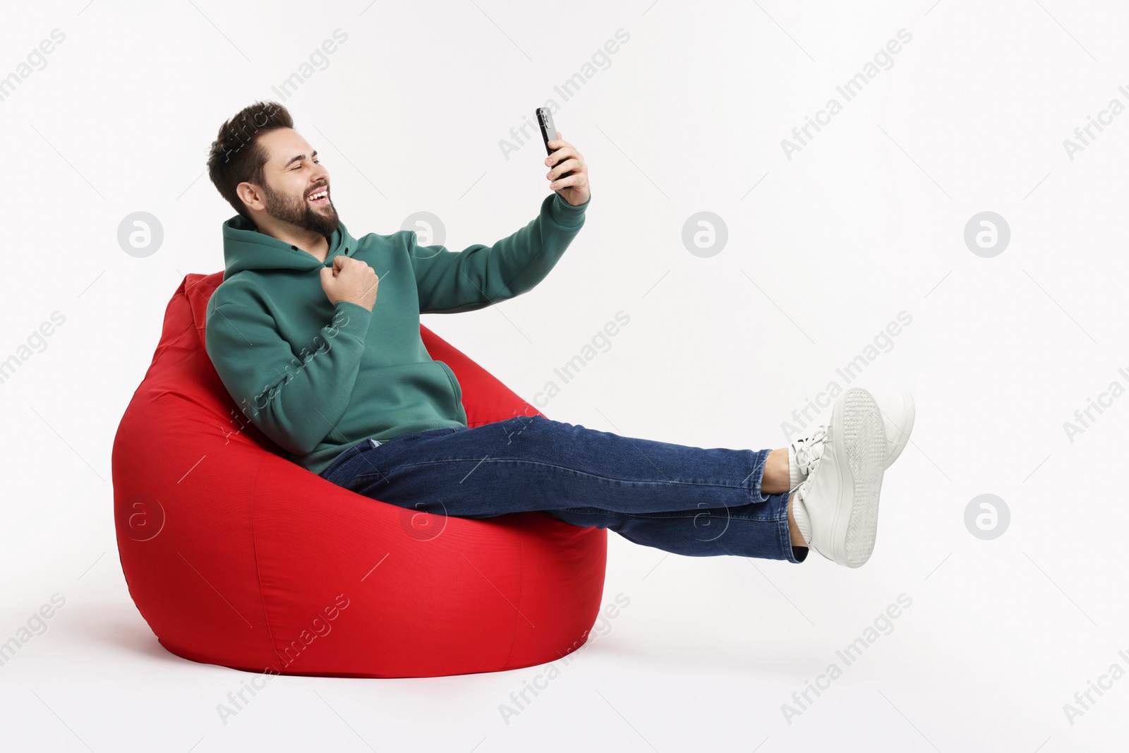 Photo of Happy young man using smartphone on bean bag chair against white background