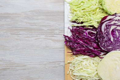 Photo of Different types of cut cabbage on white wooden table, top view. Space for text