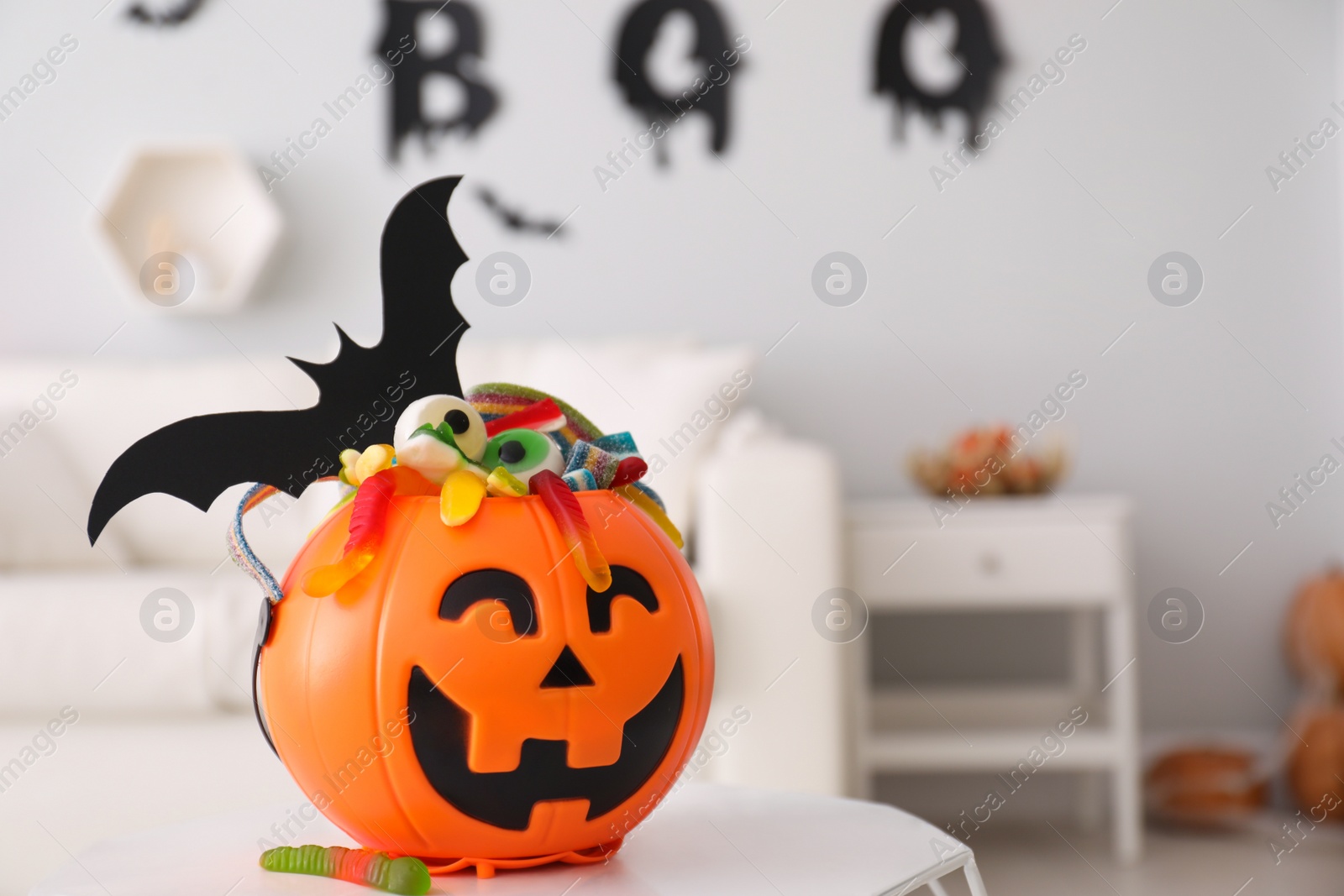 Photo of Halloween trick or treat bucket with different sweets on white table indoors