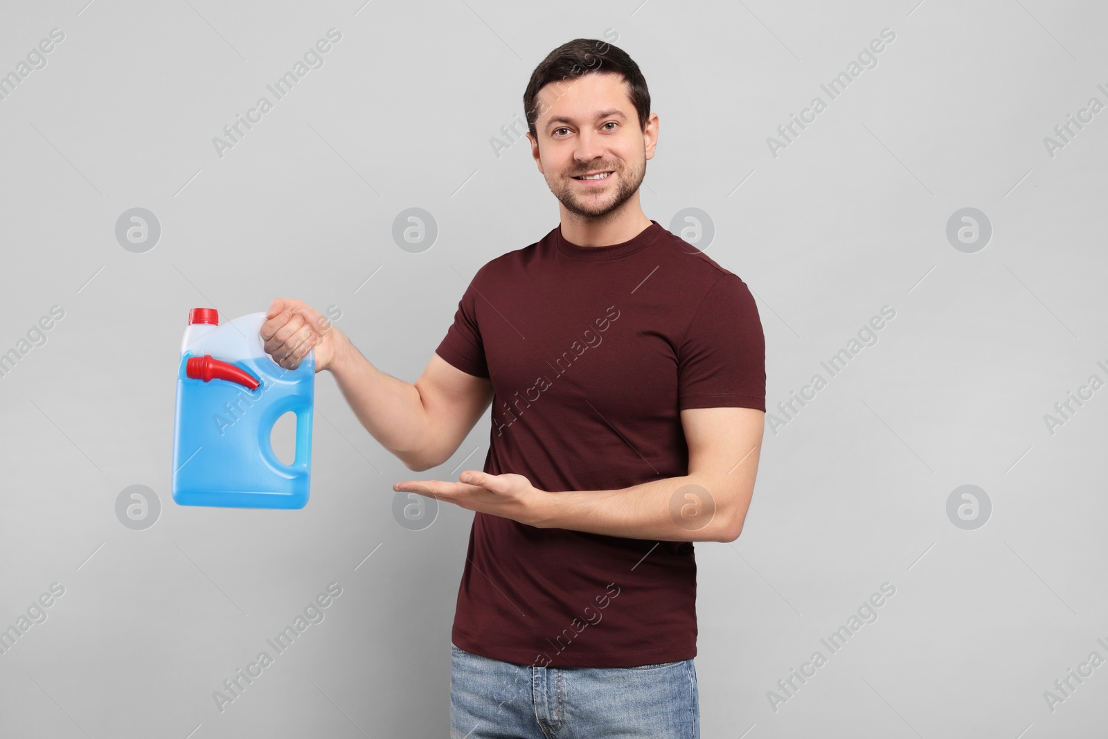 Photo of Handsome man showing canister with blue liquid on light grey background