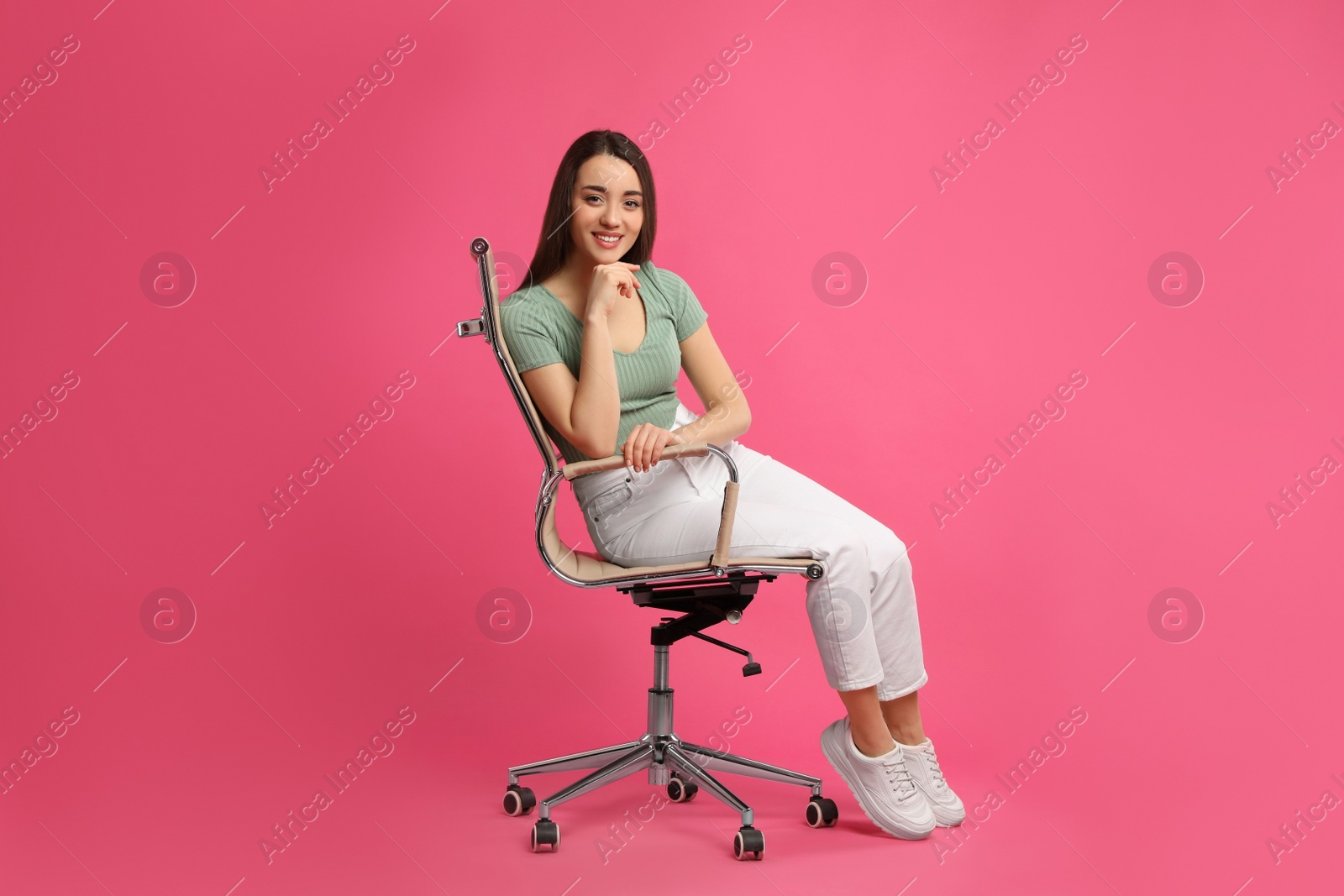 Photo of Young woman sitting in comfortable office chair on pink background