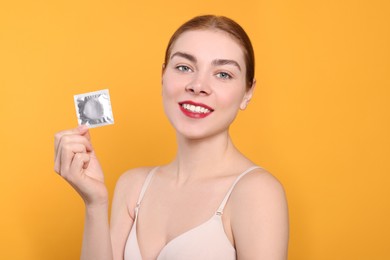 Photo of Woman in bra holding condom on yellow background. Safe sex