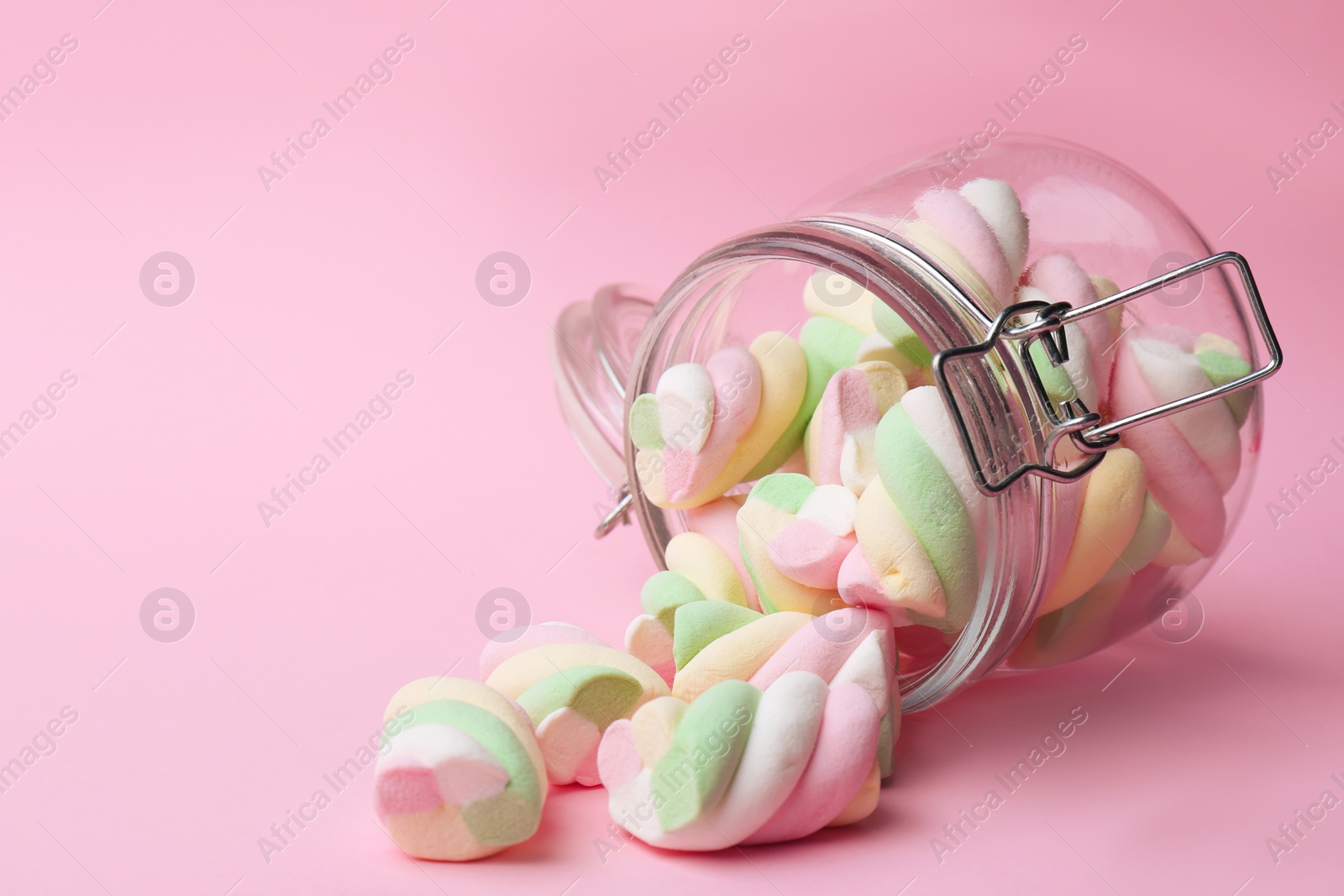 Photo of Overturned jar with delicious colorful marshmallows on pink background, space for text