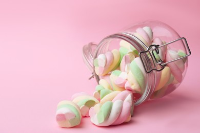 Photo of Overturned jar with delicious colorful marshmallows on pink background, space for text