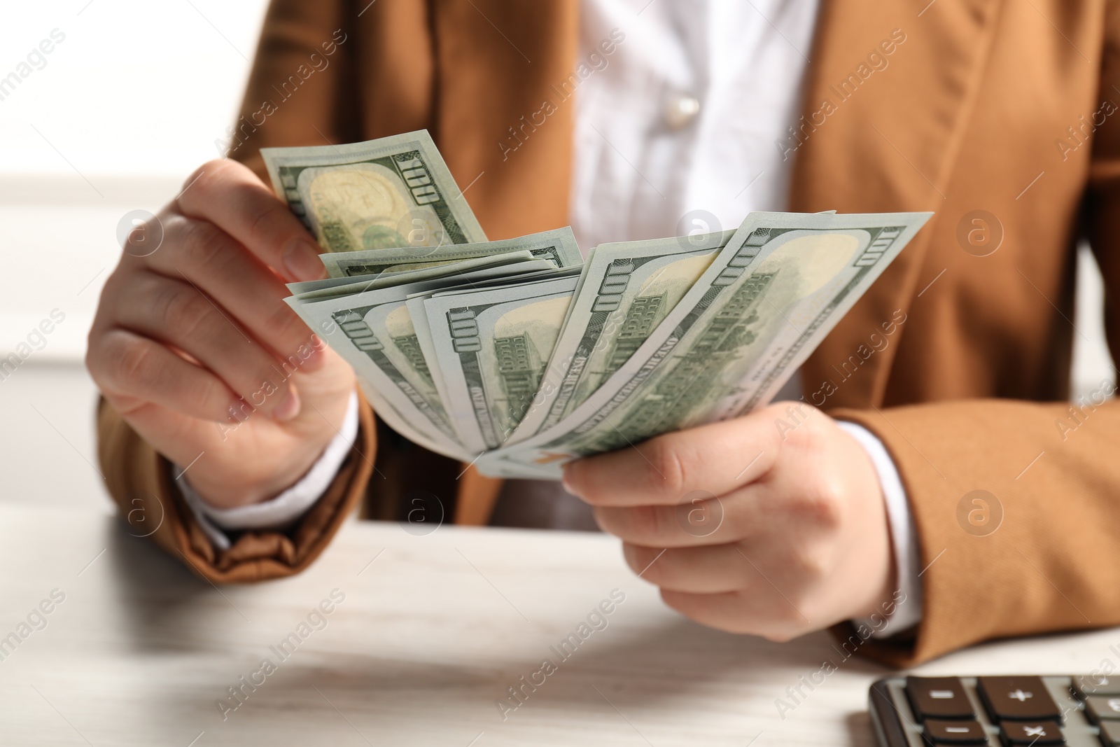 Photo of Money exchange. Woman holding dollar banknotes at white wooden table, closeup