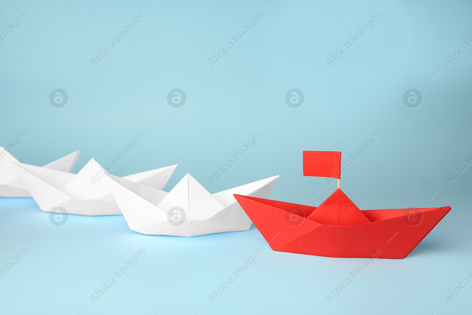 Photo of Group of paper boats following red one on light blue background. Leadership concept