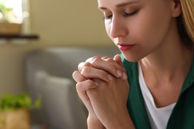 Photo of Religious young woman with clasped hands praying indoors, closeup. Space for text