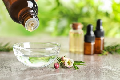 Photo of Dripping natural tea tree oil from bottle into bowl on table, space for text