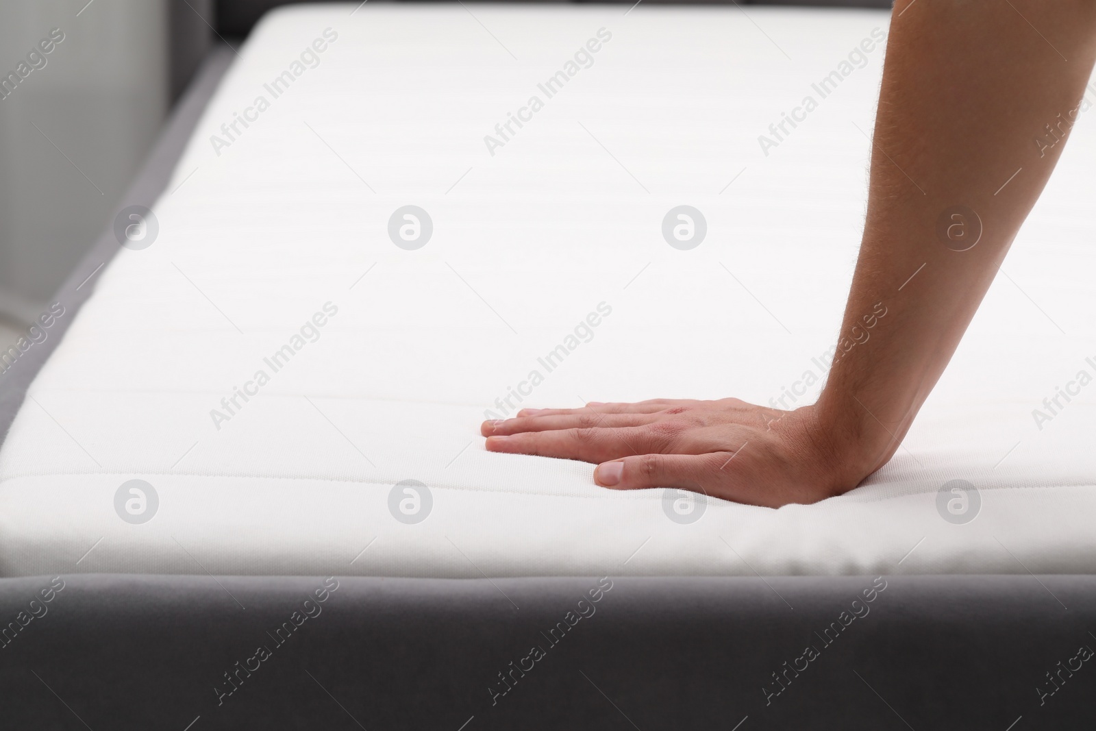 Photo of Man touching soft mattress with bed sheet, closeup