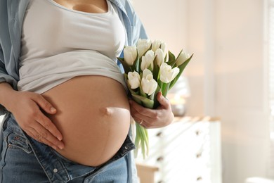 Photo of Young pregnant woman with flowers indoors, closeup. Space for text