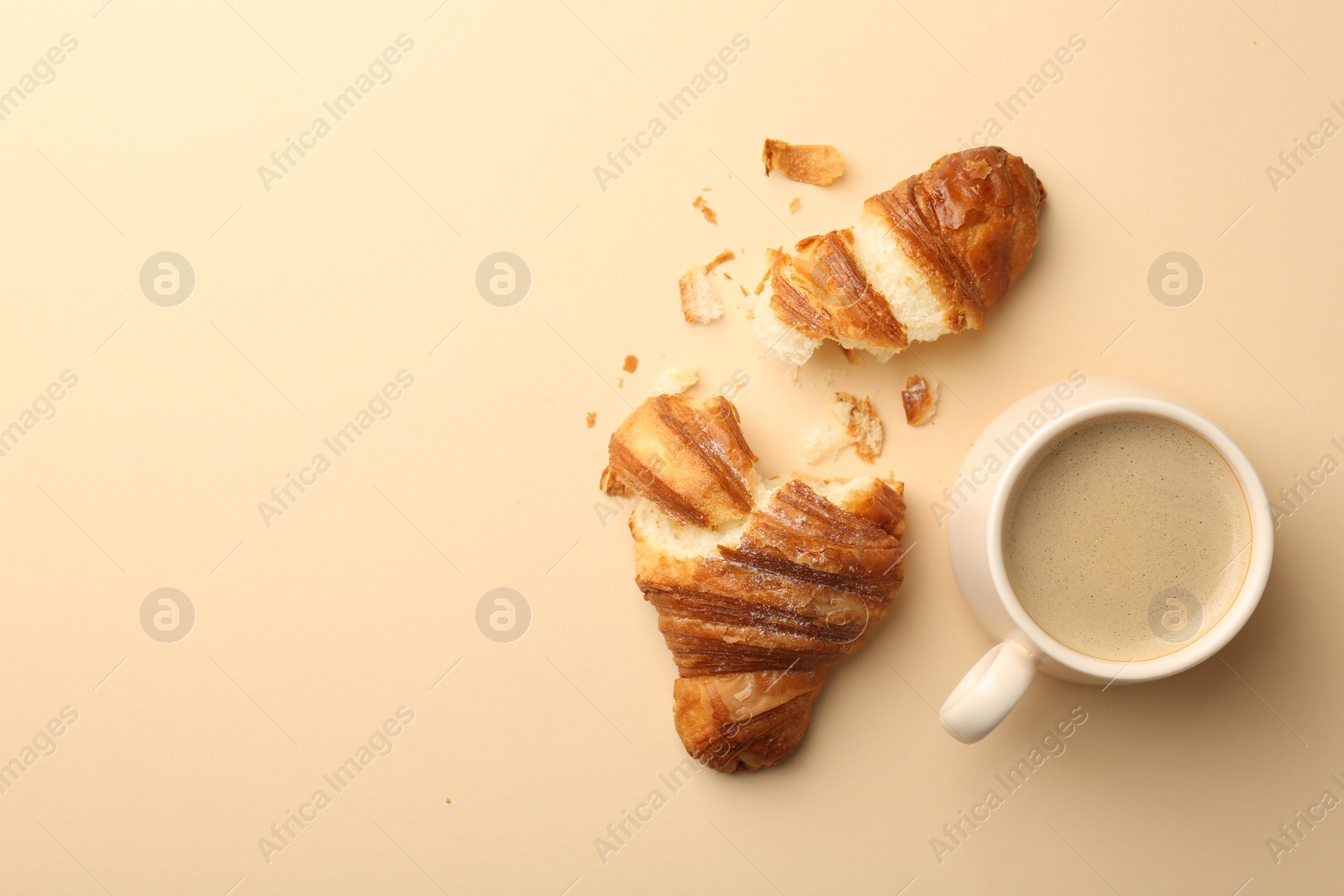Photo of Delicious croissant and cup of coffee on beige table, flat lay. Space for text